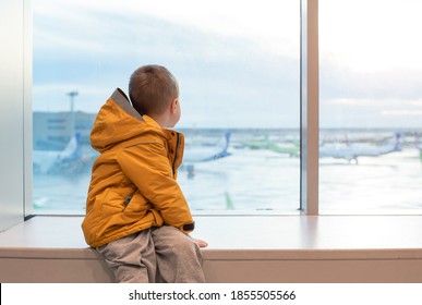 A boy in a yellow jacket at the airport at the big window.