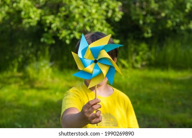 A boy in a yellow jersey plays with a yellow and blue paper 8-petal weather vane in the garden. Children's creativity