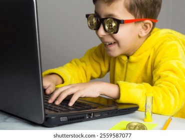 Boy in yellow pajamas and wearing glasses with bitcoin sits at the computer, earning on Bitcoin mining. The child learns to make money. - Powered by Shutterstock