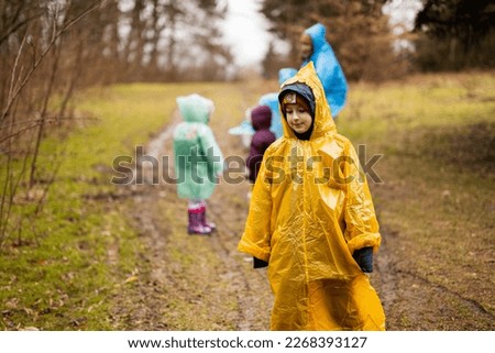 Boy in yellow raincoat against mother and children in the forest after rain in raincoats together.