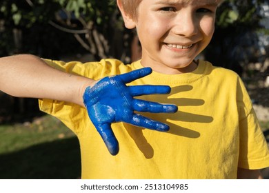 boy in a yellow T-shirt shows his hand painted blue, thus creating the flag of Ukraine. Independence Day of Ukraine. Patriotic concept. Children of Ukraine are against war - Powered by Shutterstock