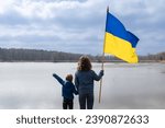 boy and young woman, younger brother and adult sister, stand next to each other holding hands with large flag of Ukraine. Back view. Family, unity, refugees, support. day of dignity and freedom