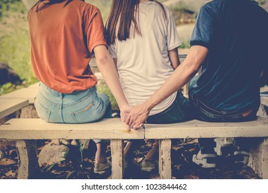 Boyfriend and another woman grab hands from behind together without sight of his girlfriend.. Paramour and divorce concept. Social problem and cheating couples theme. Teen adult and University theme.