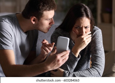 Boyfriend asking for an explanation to his cheater sad girlfriend sitting on a couch in the living room in a house interior with a dark background