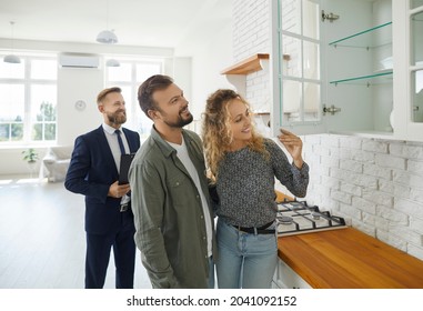 Boyfriend and girlfriend buying house. First time buyers or future tenants meeting real estate agent and looking around new home. Husband and wife looking at good quality modern wooden kitchen cabinet