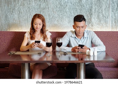 Boyfriend and girlfriend drinking wine, waiting for food and checking social media on smartphones