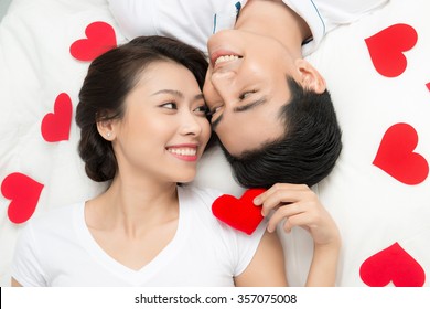 Boyfriend And Girlfriend Lying Taking Selfie With Happy Face Expression Looking Each Other In Eyes. Couple Of Asian Lovers At The Beginning Of Love Story Having Fun Together.