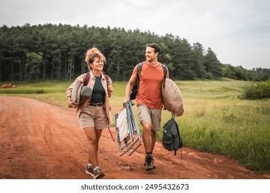 Boyfriend and girlfriend walk on dirt road with camp equipment - Powered by Shutterstock