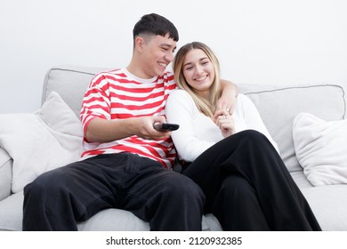 Boyfriend And Girlfriend Watching TV Smiling. Guy Using The Remote Control. Young Couple At Home. Heterosexual 18-20 Years Old Couple.