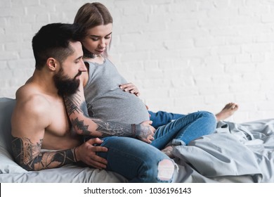 boyfriend hugging pregnant tattooed girlfriend at home
