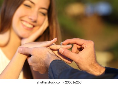 Boyfriend Putting A Engagement Ring In His Girlfriend Finger Outdoors With The Smile Of The Girl In The Background