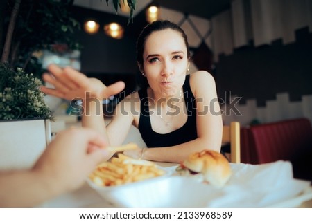 
Boyfriend Stealing French Fries from Unhappy Hungry Girlfriend. Unhappy woman not willing to share her meal with her date
