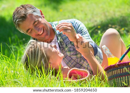 Boyfriend teasing his girlfriend with a grass twig while on a picnic in the countryside
