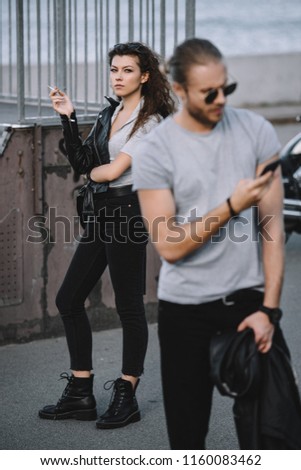 boyfriend using smartphone while girlfriend standing with classical motorcycle on background