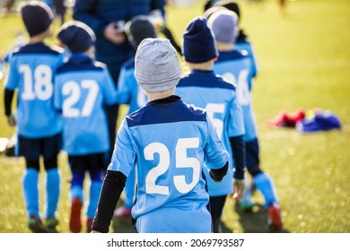 Boys In Blue Soccer Jersey Shirts Following Coach In A Team. Tournament Match For School Kids. Children Playing Sports Outdoor In WInter Sunny Day. Kids In Soccer Winter Clothing