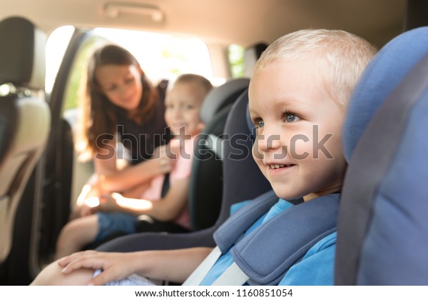 Boys buckled into car\
seat. Mother takes care about her children in a car. Safe family\
travel concept