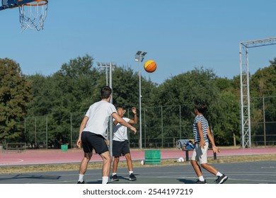 Boys engage in outdoor basketball training with a coach, practicing dribbling, passing, and shooting skills on a court surrounded by greenery under bright natural light, fostering teamwork  - Powered by Shutterstock