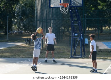 Boys engage in an outdoor basketball training session led by a coach, practicing techniques and building teamwork. The coach instructs them in skills, fostering discipline and fitness in a fun setting - Powered by Shutterstock