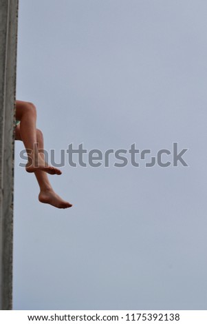 Boy's feet dangle over edge of concrete ledge, under a grey sky.