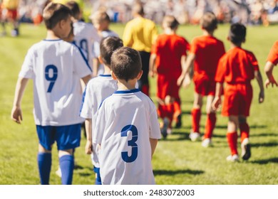 Boys in football shirts enter the field in two rows. Kids play school soccer tournament. Children compete in two football teams outdoors - Powered by Shutterstock