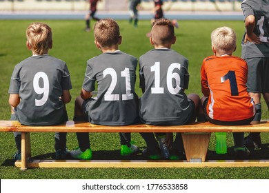 Boys In Football Team Sitting On Substitute Bench Ready To Play The Final Tournament Match. School Kids In Sports Uniforms With Player Numbers On Backs. Soccer Players In School Junior Level Team