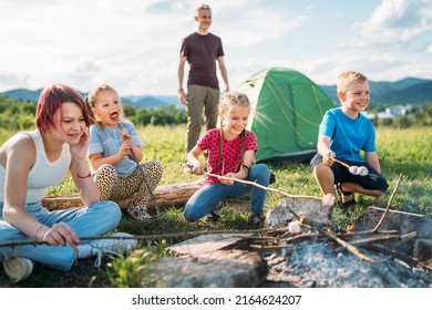 Boys and girls friends kids cheerfully laughing and roasting marshmallows on sticks over campfire flame near the green tent. Outdoor active time spending or camping in Nature concept. - Powered by Shutterstock