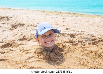 the boy's head sticks out of the sand. Fun weekend at the seaside. - Powered by Shutterstock