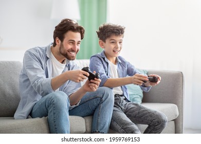 Boys Are Boys. Joyful Father And Teen Son Competing With Each Other In Online Video Games, Using Joysticks, Having Fun At Home While Sitting On Sofa And Enjoying Time Together