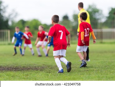 Boys Kicking Football On The Sports Field