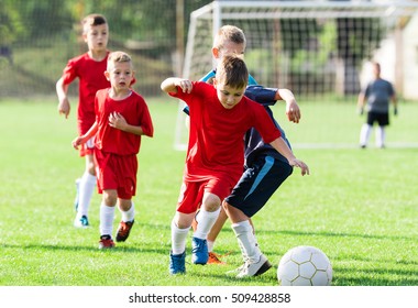 Boys Kicking Football On The Sports Field