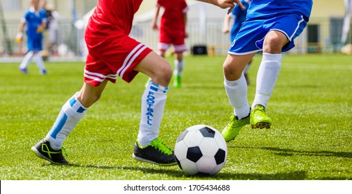 Boys Playing Football Game. Kids Running After Ball. Junior Level Soccer Tournament Match Outdoor. Competition Between Players In Red And Blue Jersey Shirts