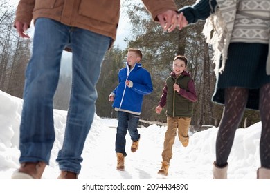 Boys Running Behind Parents Holding Hands In Snow