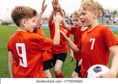 A Boys Soccer Team Celebrating A Victory. Motivated Children Sports Team Rising Hands Up. Young School Football Team On The Outdoor Grass Pitch. Happy Kids Playing Sports