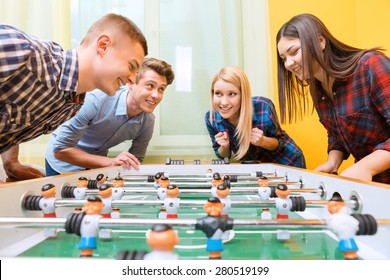 Boys Vs Girls. Young Smiling Boy Playing Air Hockey Against Young Asian Girl Watching The Play While Their Friends Standing Near And Cheering Them Up