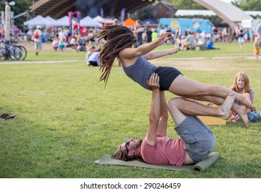 Bozeman, Montana/USA - JUNE 23,2015: A Couple Practice Acrayoga In The Park During The Summer Farmers Market. The Man Is Balancing The Woman Using Technique And Strength.