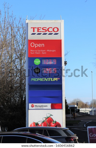 Brackley, Northamptonshire, England - January 4th 2020:\
Large illuminated sign at entrance to Tesco supermarket car park\
showing company logo, opening hours and price per litre of petrol\
and diesel 