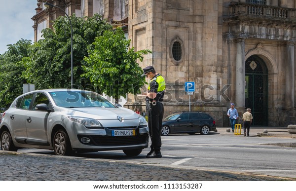 Braga,\
Portugal - May 23, 2018: policeman checks and writes a traffic\
ticket on a car in the city center on a spring\
day