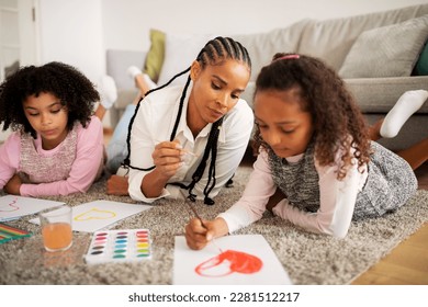 Braided African American Mother And Two Daughters Drawing Coloring Heart  Making Painting Together Lying On Floor In Modern Living Room Indoors On Weekend  Family Hobby And Leisure  Selective Focus
