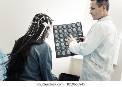 Brain Activity. Handsome Nice Skillful Doctor Standing Near His Patient And Pointing At The X Ray Scan While Explaining The Diagnosis