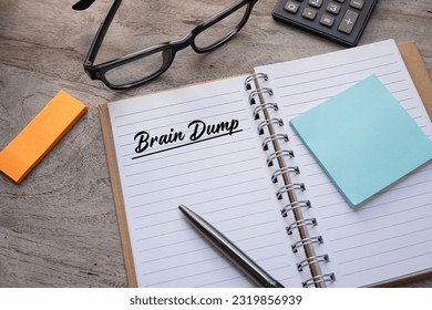 Brain Dump, two words were written on the notebook on the wooden table, with a pen, post-it note, eyeglasses, and calculator. Business and in-discussion concept