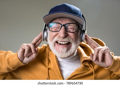 Its Brain Explosion. Portrait Of Cheerful Elderly Man Listen To Music On Headphones. His Eyes Are Closed With Pleasure. Isolated On Grey Background