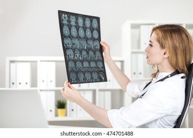 Brain Surgeon Is Looking At X Ray Images Of Her Patient Sitting At Her Workplace. Concept Of Difficult Decision Making