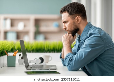 Brainstorming Concept. Young Pensive Man Sitting At Desk And Looking At Laptop Screen, Thoughtful Millennial Male Touching Chin, Entrepreneur Using Computer At Workplace, Thinking About Project