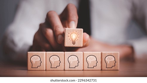 brainstorming creative idea and innovation. Hand putting over wooden cube block with light bulb icon on many people together having an idea symbolized by icons on cubes.
