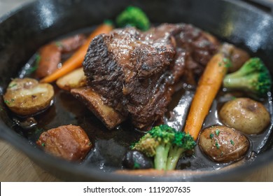 Braised Red Wine Beef Short Ribs Recipe With Vegetables And Bread In Black Pan On Wood Table.