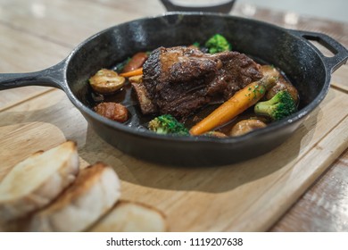 Braised Red Wine Beef Short Ribs Recipe With Vegetables And Bread In Black Pan On Wood Table.