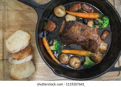 Braised Red Wine Beef Short Ribs Recipe With Vegetables And Bread In Black Pan On Wood Table.