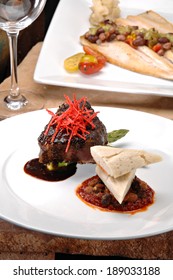 Braised Short Ribs On A Bright Red Tomato Paste Sauce.  Garnished With Avacado, Sliced Tortilla Chips And A Red Wine Reduction Sauce.  Colorful Sauteed Spinach Is Displayed Behind The Meat.