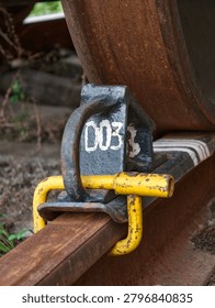 Brake chock installed beneath a rust covered train wheel on a weathered rail ensuring stability and railway safety in freight transport
