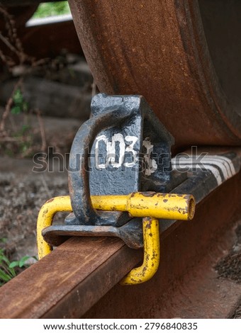 Brake chock installed beneath a rust covered train wheel on a weathered rail ensuring stability and railway safety in freight transport